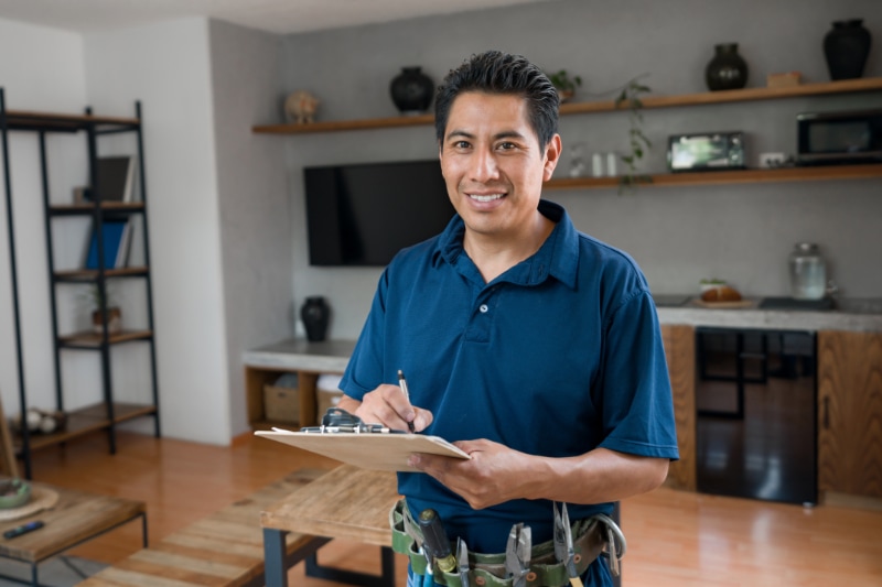 What Is a Plumbing Inspection? Happy electrician working at a house and smiling while writing on a clipboard.|Tankless vs. Traditional Water Heaters: Which is Best for Your Home?
