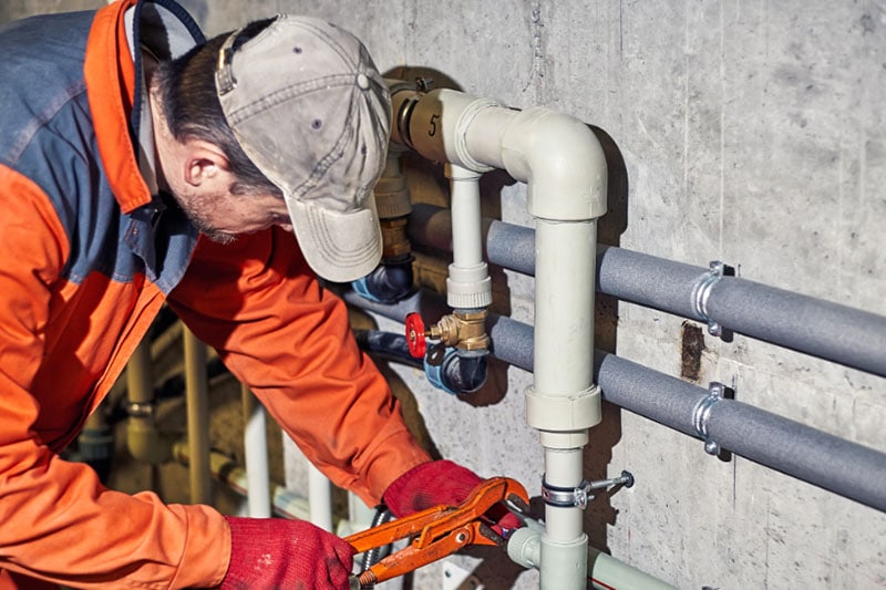 How Backflow Prevention Protects Your Business Photo of plumber performing maintenance on a pipe installed outside of a building.