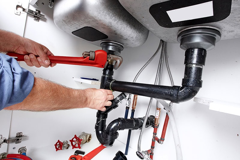 The Effects of Drain Openers on Pipes. Hands of professional Plumber with a wrench. Clogged sink.